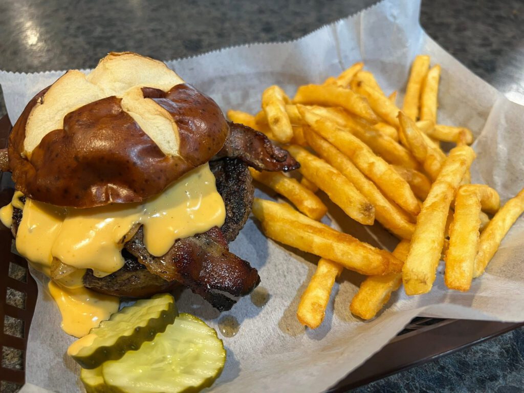 Tippy’s Burger with a half-pound beef patty topped with bacon, beer cheese sauce, and beer-braised onions on a pretzel bun.